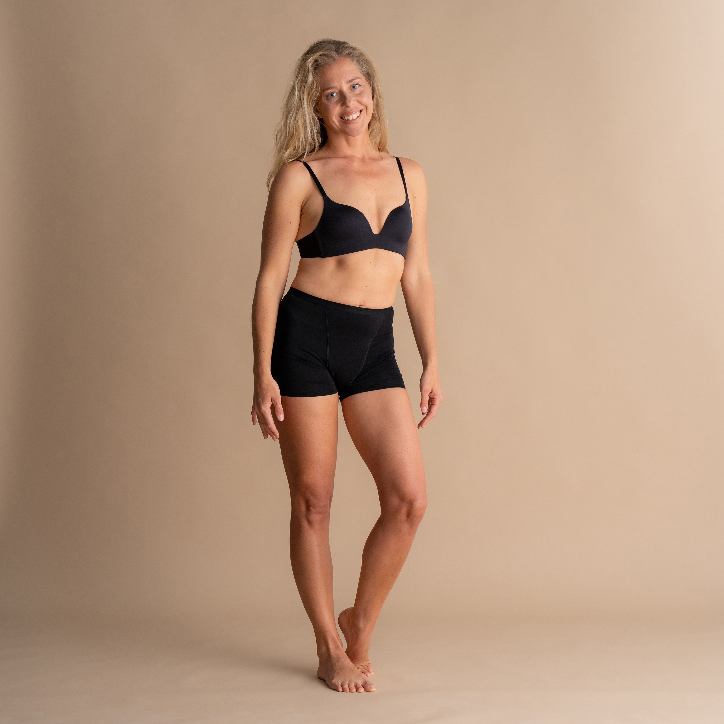 Nasmejan model v črnih Floena Leakproof Bamboo Sleep Short menstrualnih hlačkah za spanje in ujemajočem modrčku pred bež ozadjem
