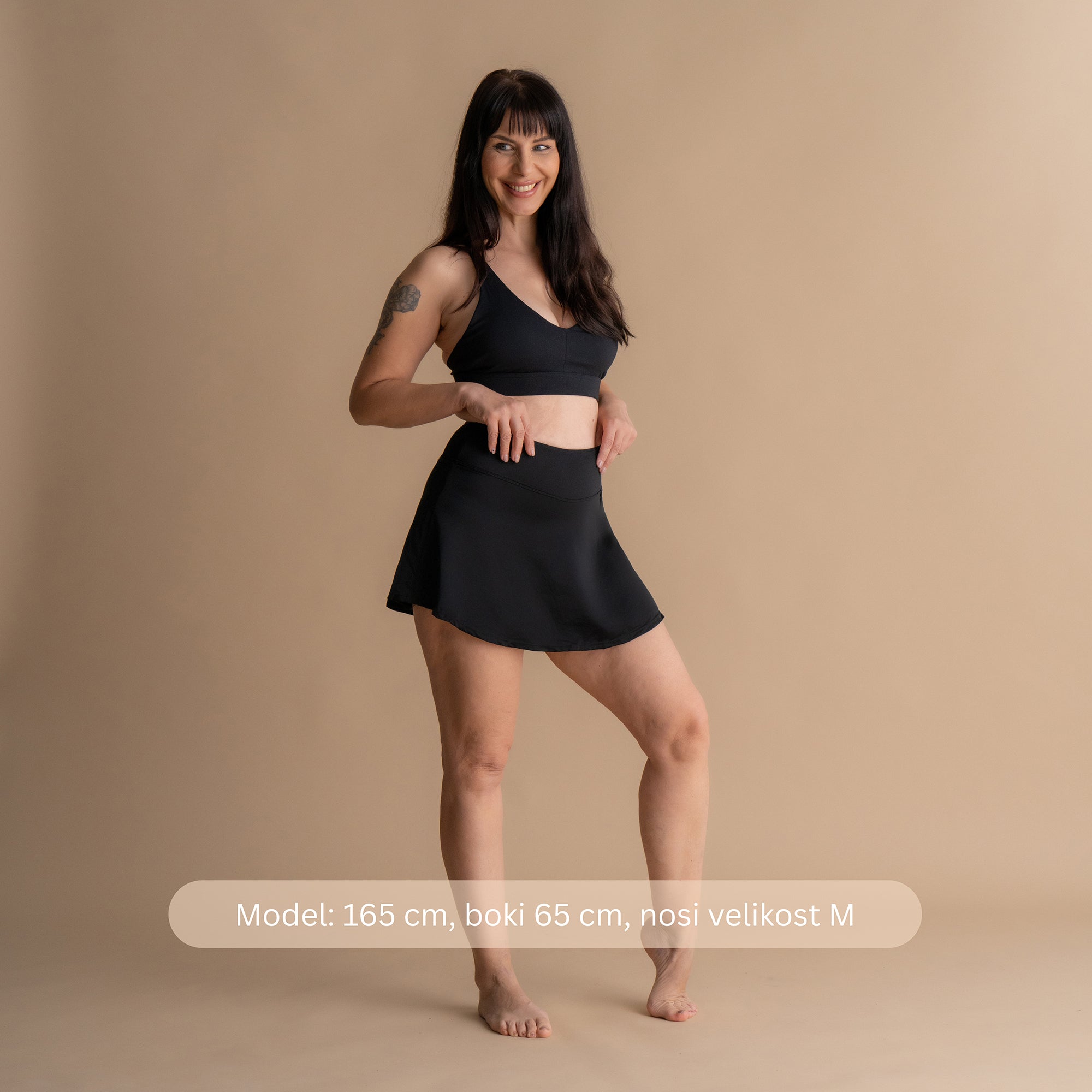Sprednji pogled na nasmejan model z rokami na bokih v črnem Floena Leakproof Period Swim Skirt, menstrualno kopalno krilo, z ujemajočim bikini zgornjim delom