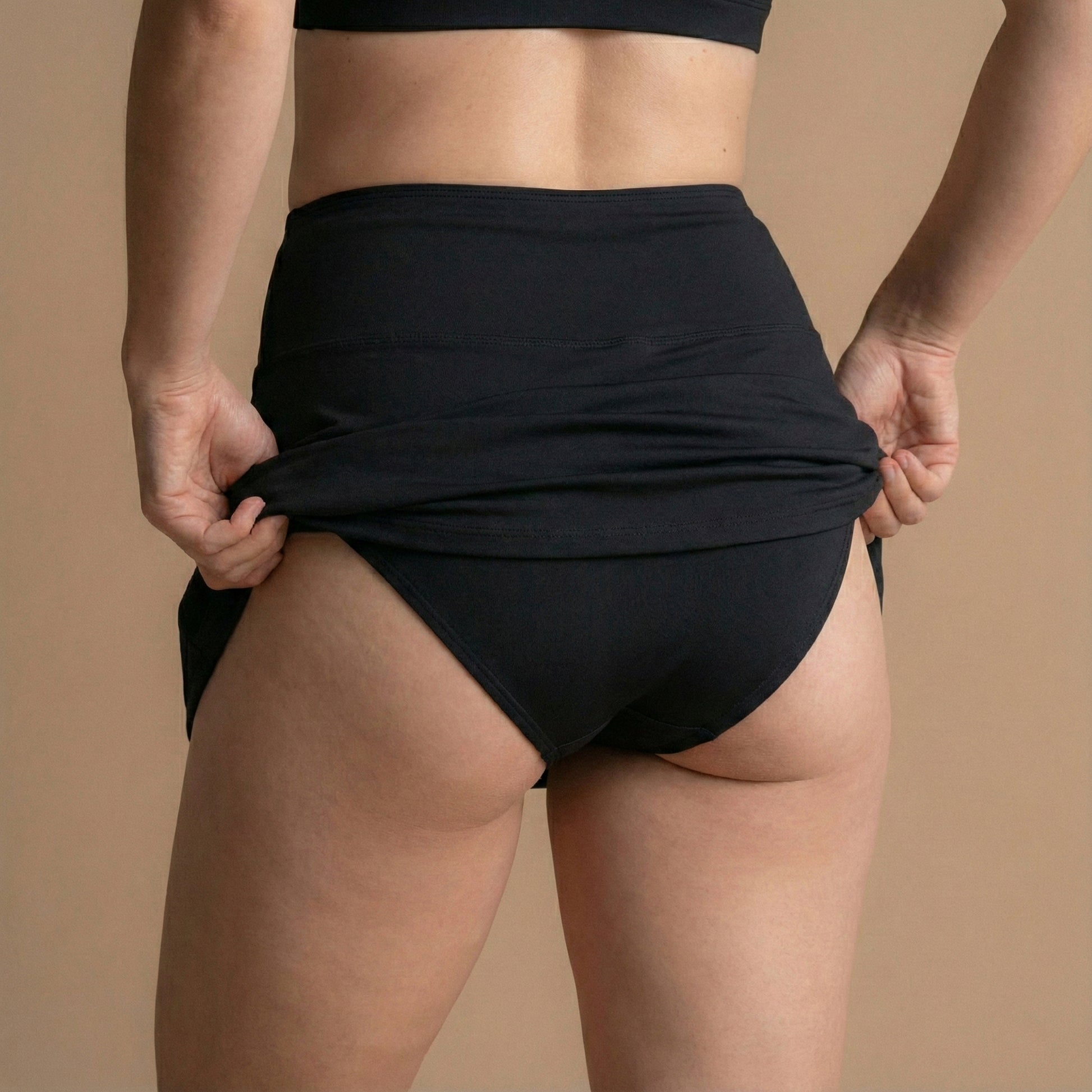 Zadnji pogled na model, ki si prilagaja črno Floena Leakproof Period Swim Skirt, menstrualno kopalno krilo, s polno pokritostjo in visokim pasom