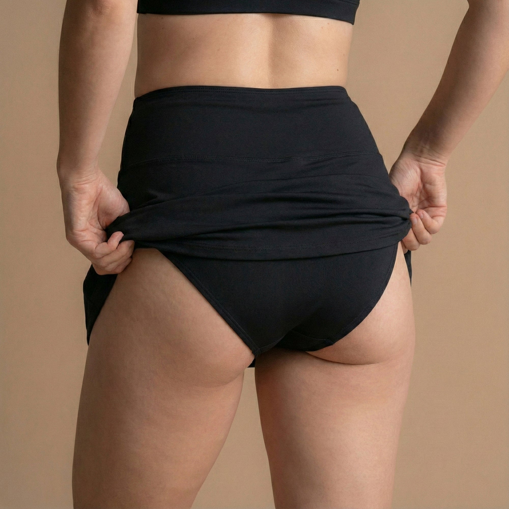 Zadnji pogled na model, ki si prilagaja črno Floena Leakproof Period Swim Skirt, menstrualno kopalno krilo, s polno pokritostjo in visokim pasom