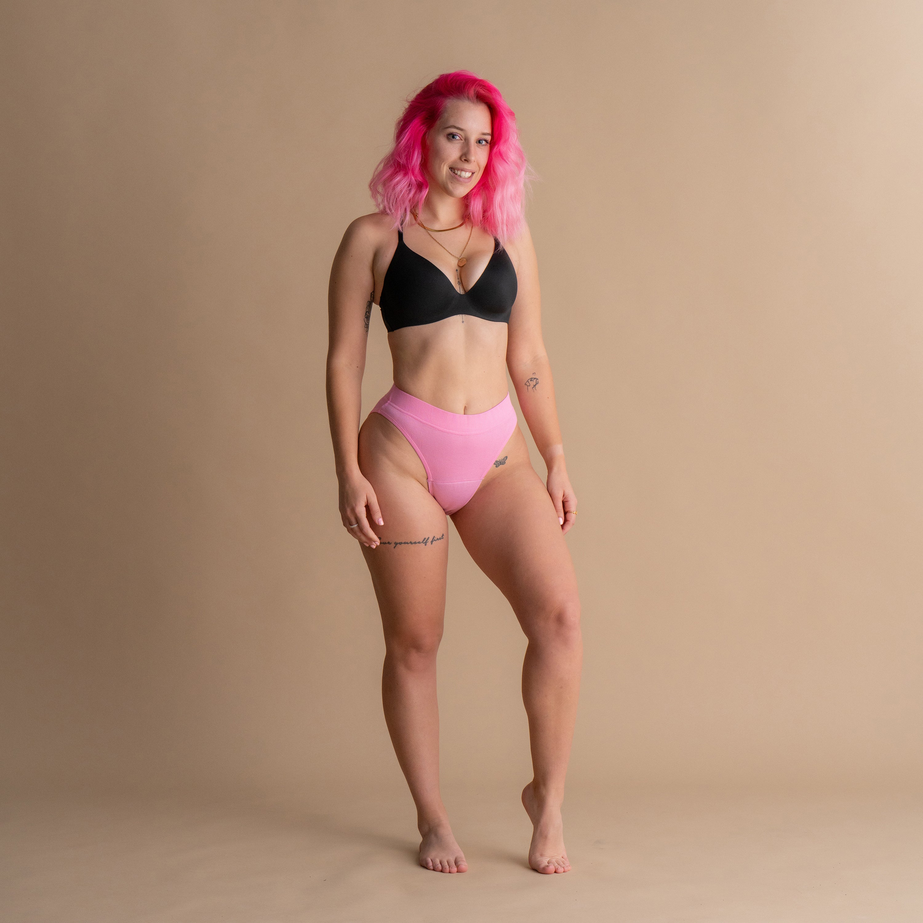 Celoten sprednji pogled na model z roza lasmi v roza Floena Leakproof Ribbed High Waist Brief, rebraste visoko pasne menstrualne hlačke, in črnem modrčku na bež ozadju
